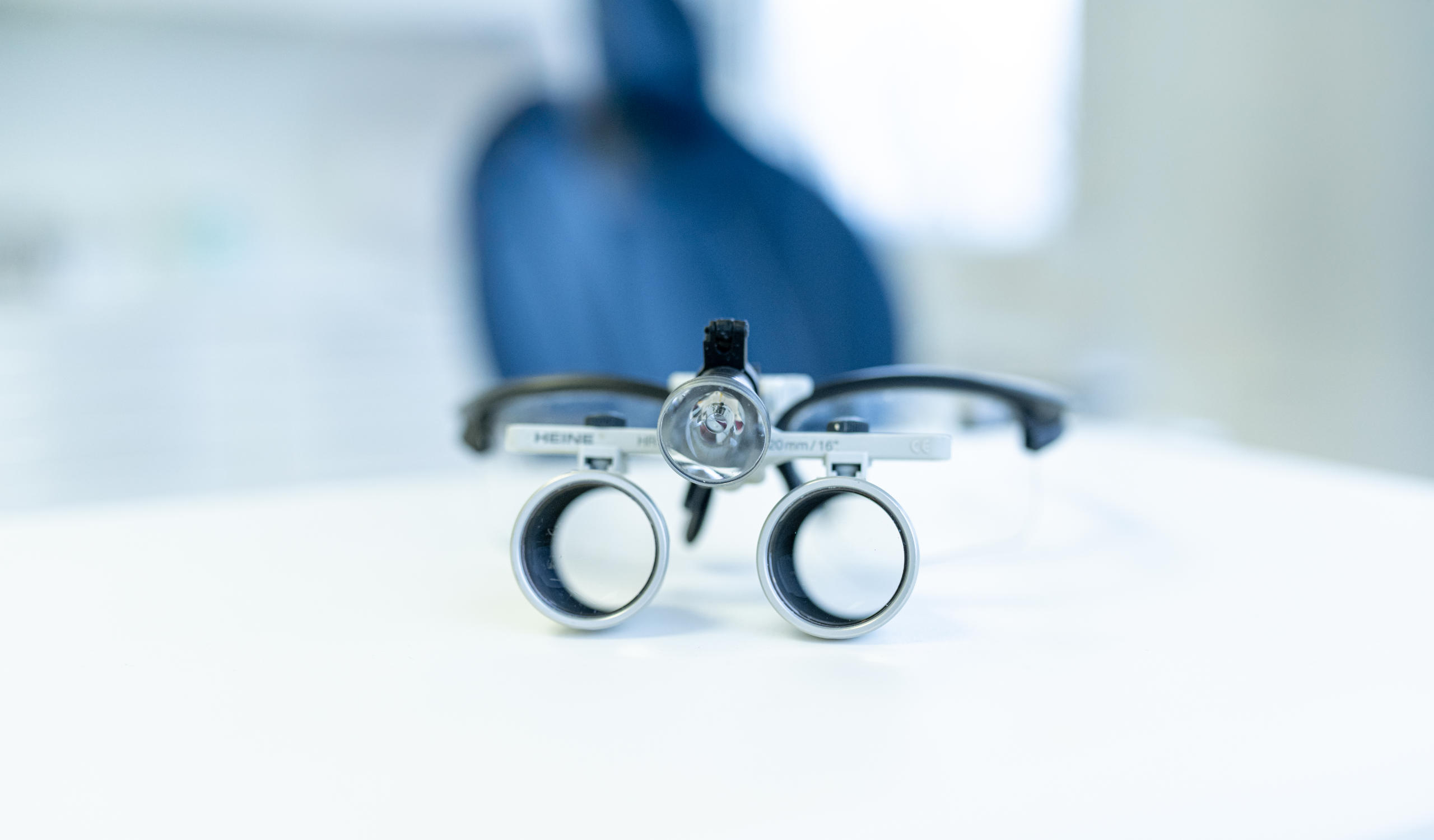 Nahaufnahme einer Zahnarztbrille auf einem weißen Tisch mit verschwommenen Hintergrund eines Behandlungsraumes